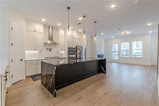 kitchen with wall chimney range hood, decorative light fixtures, a large island with sink, light hardwood / wood-style floors, and white cabinets