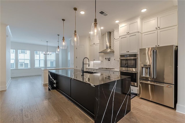 kitchen with stainless steel appliances, backsplash, white cabinets, wall chimney exhaust hood, and light hardwood / wood-style flooring