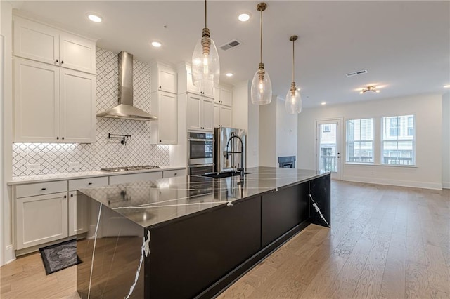 kitchen with light wood-type flooring, appliances with stainless steel finishes, stone counters, sink, and a kitchen island with sink