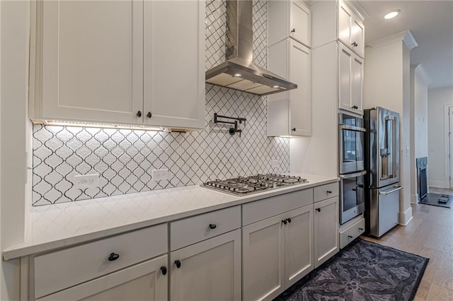 kitchen featuring stainless steel appliances, wall chimney range hood, white cabinetry, and light hardwood / wood-style flooring