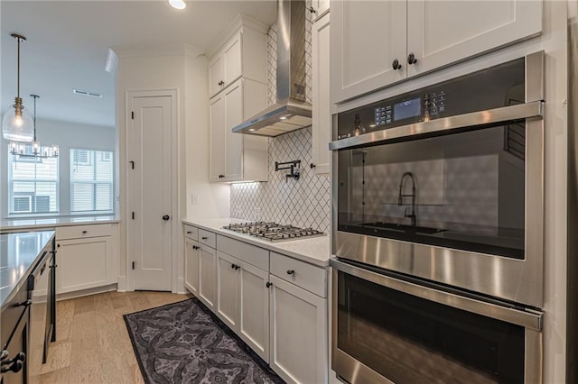 kitchen with white cabinets, appliances with stainless steel finishes, wall chimney exhaust hood, and an island with sink