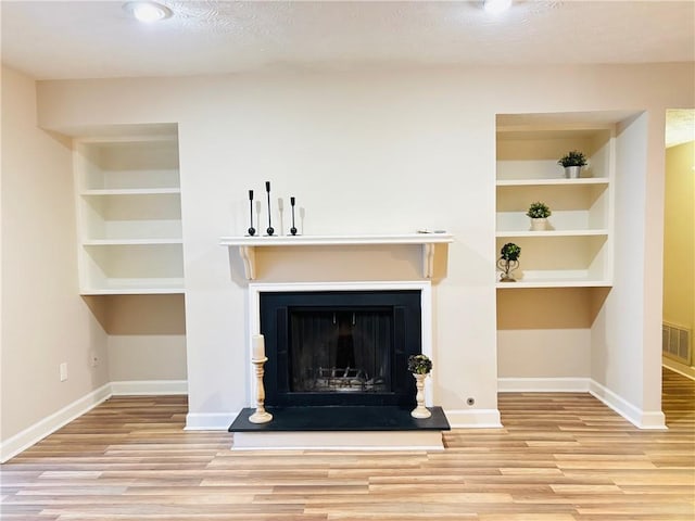 unfurnished living room featuring built in features and light wood-type flooring