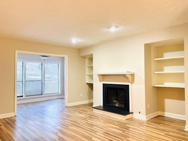 unfurnished living room featuring built in features and light wood-type flooring