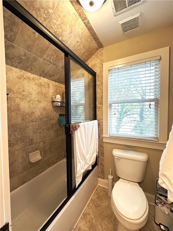 bathroom with combined bath / shower with glass door, tile patterned floors, and toilet