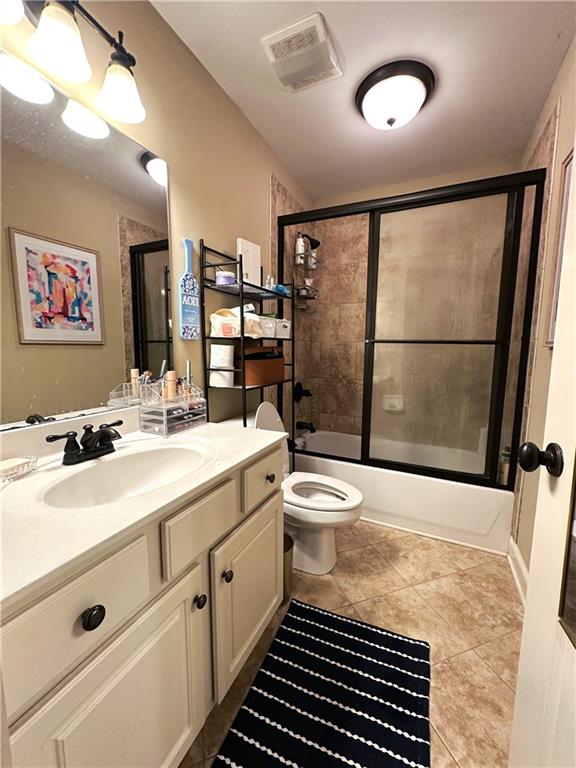 full bathroom with combined bath / shower with glass door, tile patterned floors, vanity, and toilet