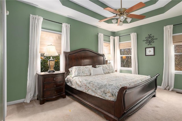 bedroom with carpet flooring, multiple windows, baseboards, and a tray ceiling