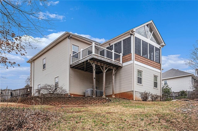 exterior space with central AC unit, fence, a wooden deck, a sunroom, and a lawn