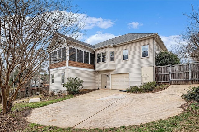 rear view of property with a garage, a sunroom, driveway, and fence