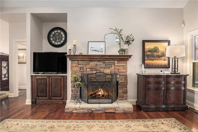 living area featuring a stone fireplace, wood finished floors, and baseboards