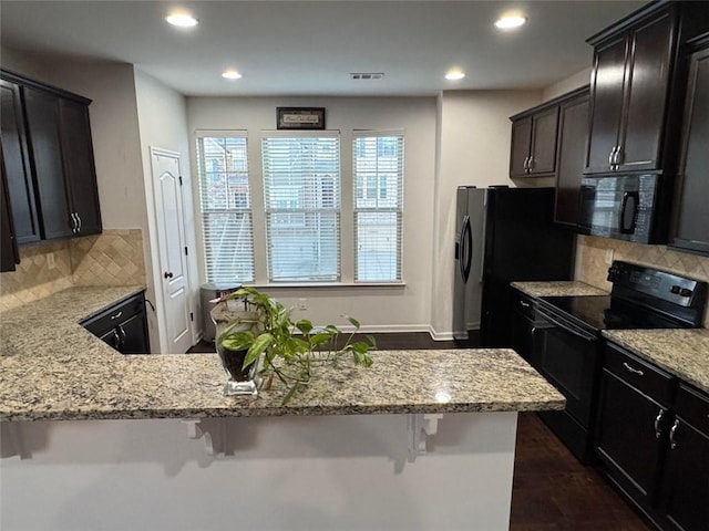 kitchen with a kitchen breakfast bar, light stone countertops, and black appliances