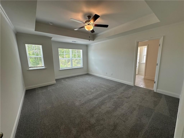 carpeted empty room featuring a ceiling fan, baseboards, ornamental molding, and a raised ceiling