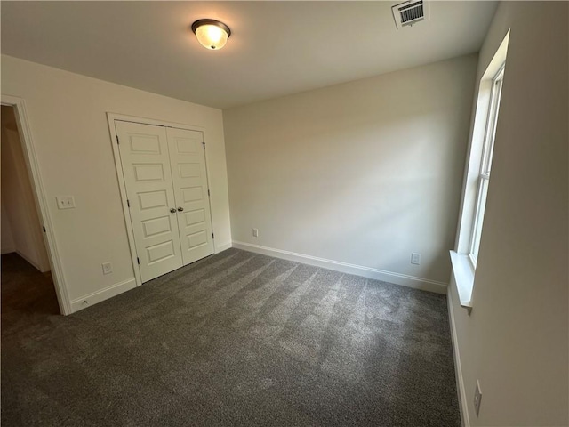 unfurnished bedroom with baseboards, visible vents, dark carpet, and a closet