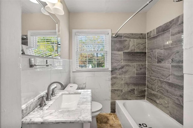 full bathroom featuring vanity, tiled shower / bath combo, toilet, and tile walls