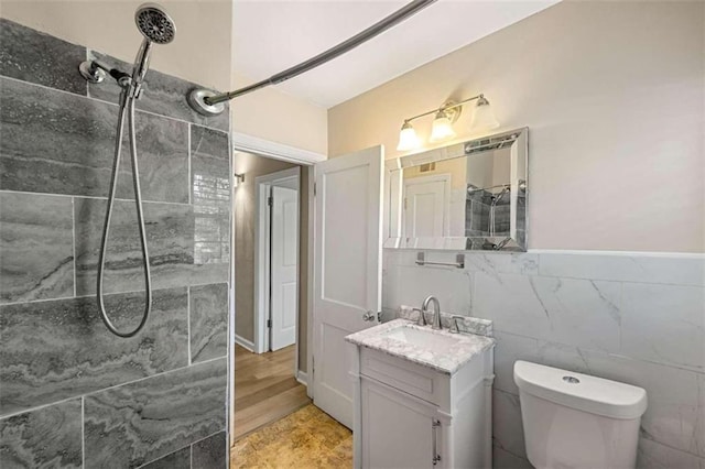 bathroom with toilet, tiled shower, vanity, tile walls, and hardwood / wood-style flooring