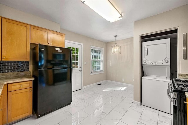 kitchen with black refrigerator, backsplash, stacked washing maching and dryer, pendant lighting, and stainless steel range with gas cooktop