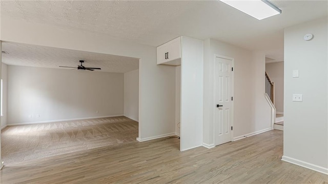 unfurnished room featuring a textured ceiling, a ceiling fan, baseboards, stairway, and light wood-type flooring