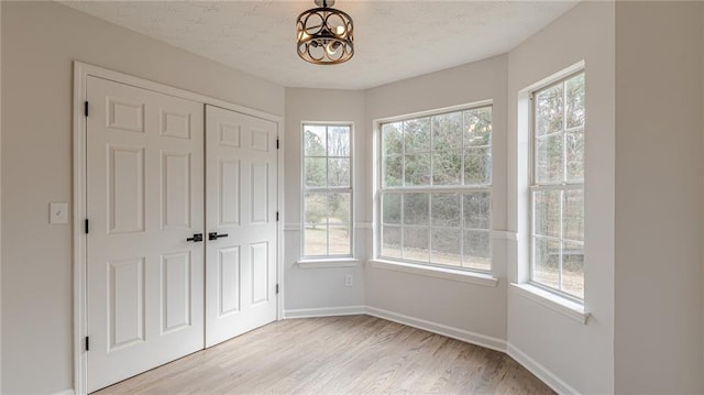 unfurnished bedroom featuring light wood-type flooring, multiple windows, and baseboards