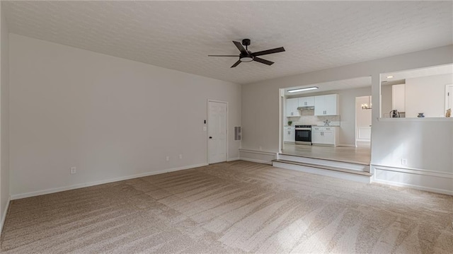 unfurnished living room featuring ceiling fan, baseboards, a textured ceiling, and light colored carpet