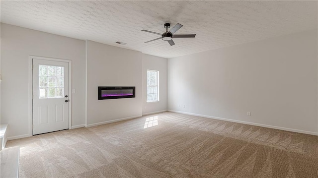 unfurnished living room featuring light carpet, a glass covered fireplace, and a wealth of natural light