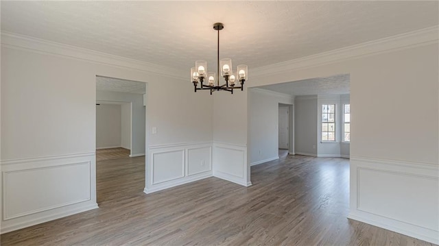 unfurnished room featuring crown molding, a decorative wall, an inviting chandelier, and wood finished floors