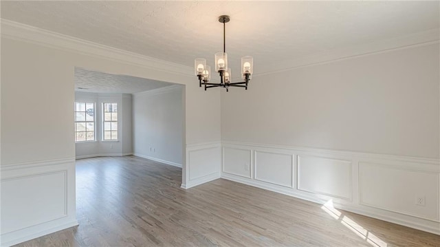 unfurnished room featuring a textured ceiling, a decorative wall, light wood-type flooring, an inviting chandelier, and crown molding