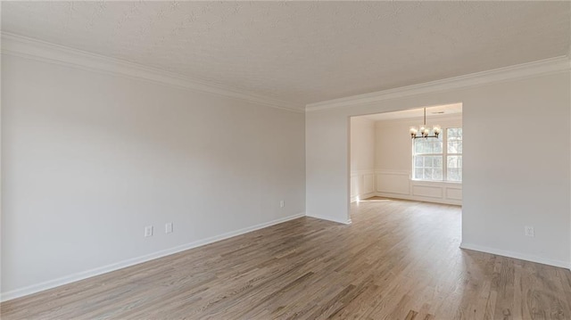 spare room with a textured ceiling, ornamental molding, wood finished floors, and a notable chandelier