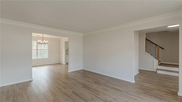 empty room with ornamental molding, stairway, wood finished floors, and an inviting chandelier