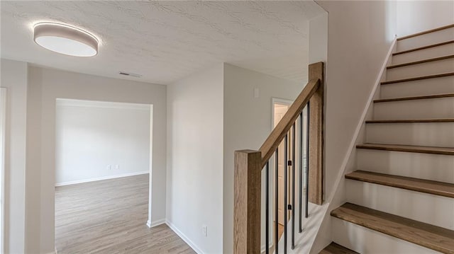 stairs with visible vents, a textured ceiling, baseboards, and wood finished floors