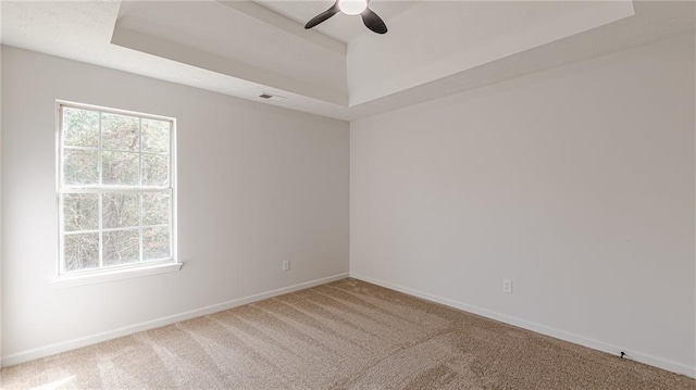 unfurnished room featuring a tray ceiling, visible vents, a ceiling fan, carpet flooring, and baseboards