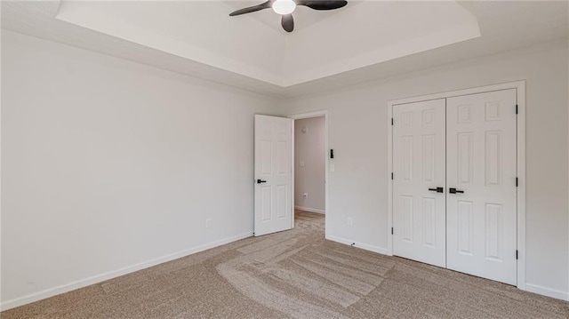 unfurnished bedroom featuring a tray ceiling, a closet, carpet flooring, and baseboards