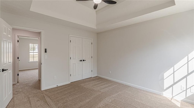 unfurnished bedroom with carpet flooring, a raised ceiling, and baseboards