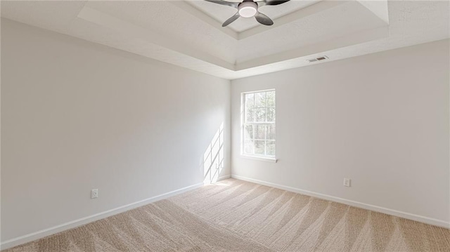 spare room with a raised ceiling, visible vents, a ceiling fan, light carpet, and baseboards