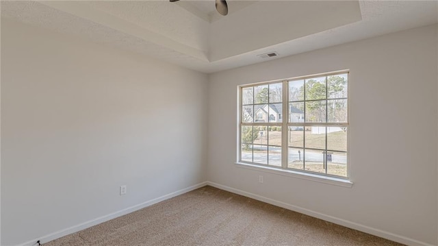 carpeted spare room featuring a healthy amount of sunlight, baseboards, visible vents, and a tray ceiling