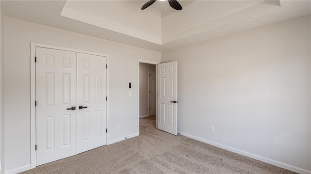 unfurnished bedroom with a closet, a raised ceiling, light colored carpet, and baseboards