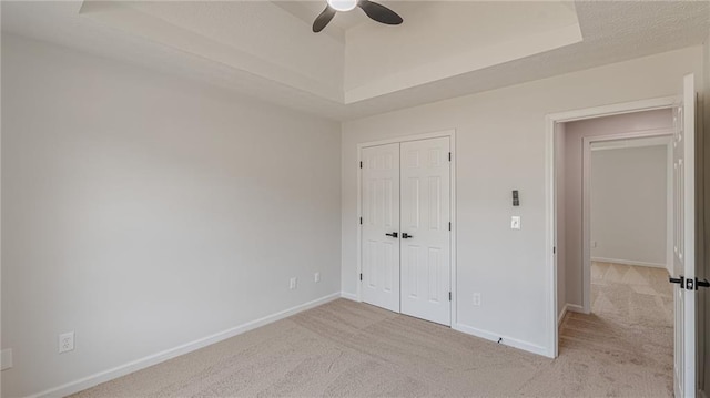 unfurnished bedroom with a closet, a raised ceiling, light colored carpet, and baseboards