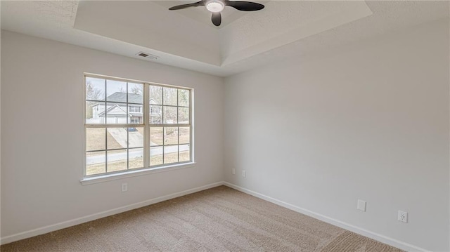 unfurnished room featuring carpet flooring, a ceiling fan, visible vents, baseboards, and a tray ceiling