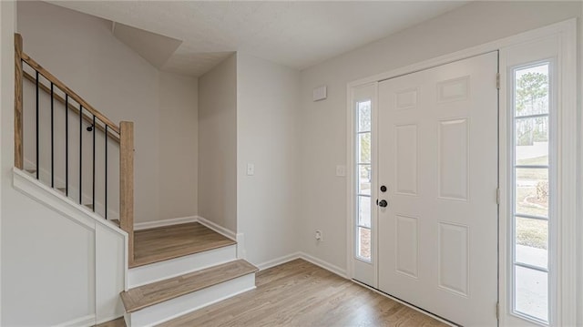 foyer entrance featuring a healthy amount of sunlight, light wood-style flooring, baseboards, and stairs