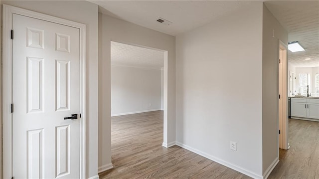 hall featuring baseboards, a textured ceiling, visible vents, and wood finished floors