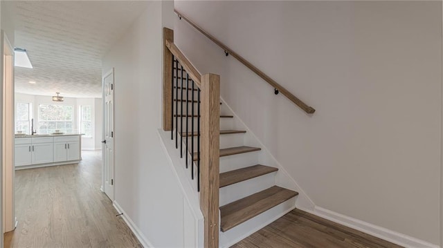 stairs with a textured ceiling, baseboards, and wood finished floors