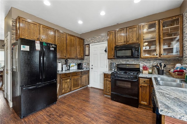 kitchen featuring sink, backsplash, dark hardwood / wood-style flooring, black appliances, and light stone countertops