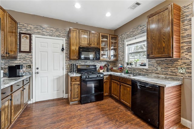 kitchen with sink, light stone counters, black appliances, dark hardwood / wood-style flooring, and decorative backsplash