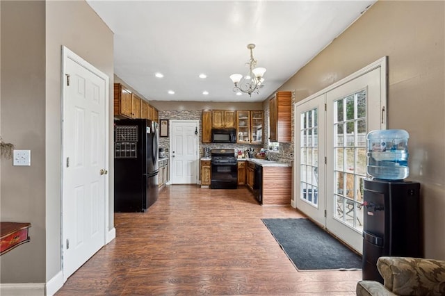 kitchen with dark wood-type flooring, black appliances, decorative backsplash, decorative light fixtures, and a chandelier