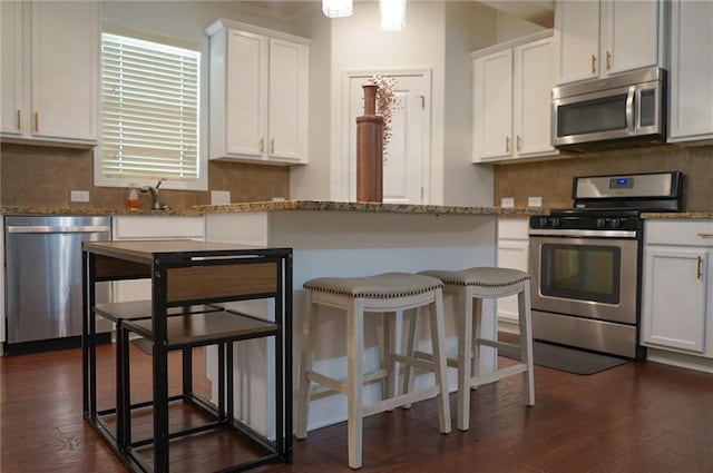 kitchen with light stone counters, dark wood-style flooring, stainless steel appliances, decorative backsplash, and white cabinets