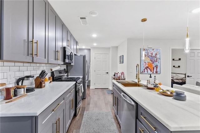 kitchen with dark wood-type flooring, sink, gray cabinets, decorative light fixtures, and stainless steel appliances