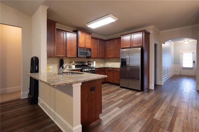 kitchen with arched walkways, dark wood-style floors, a peninsula, stainless steel appliances, and a sink