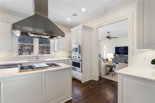 kitchen featuring island exhaust hood, a sink, backsplash, white cabinetry, and appliances with stainless steel finishes