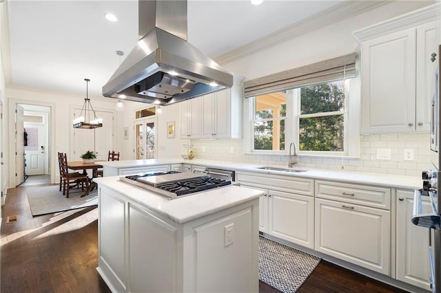 kitchen featuring dark wood-type flooring, a sink, island range hood, decorative backsplash, and stainless steel gas cooktop