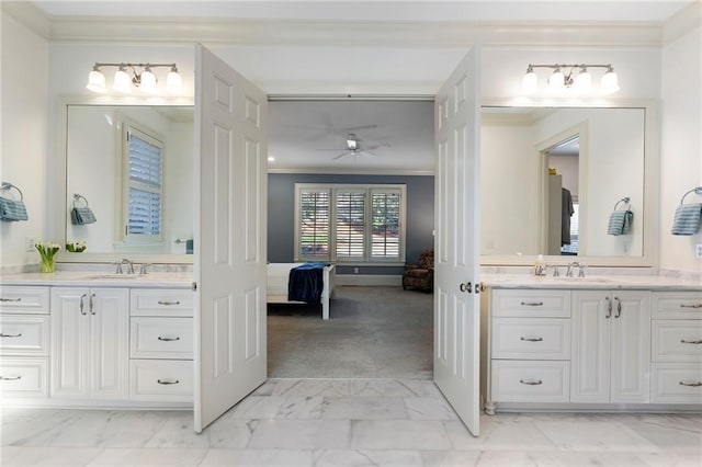 ensuite bathroom featuring two vanities, marble finish floor, crown molding, and a sink