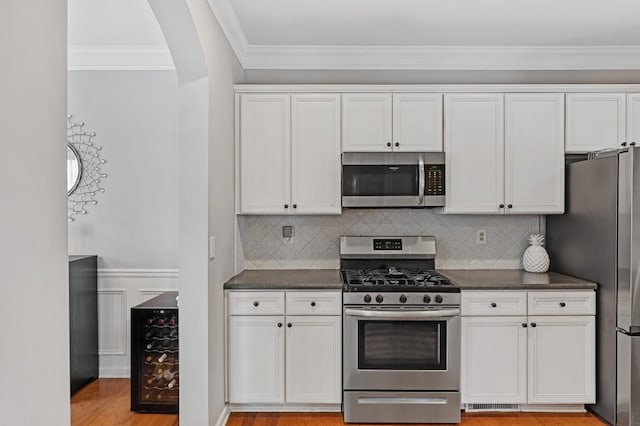 kitchen featuring white cabinetry, wine cooler, dark stone counters, ornamental molding, and stainless steel appliances