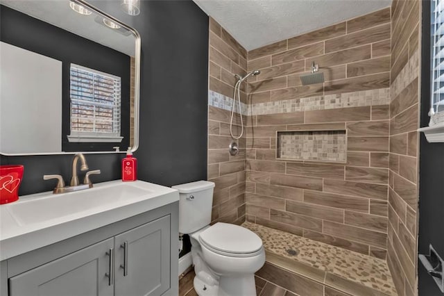 bathroom with toilet, a tile shower, and vanity